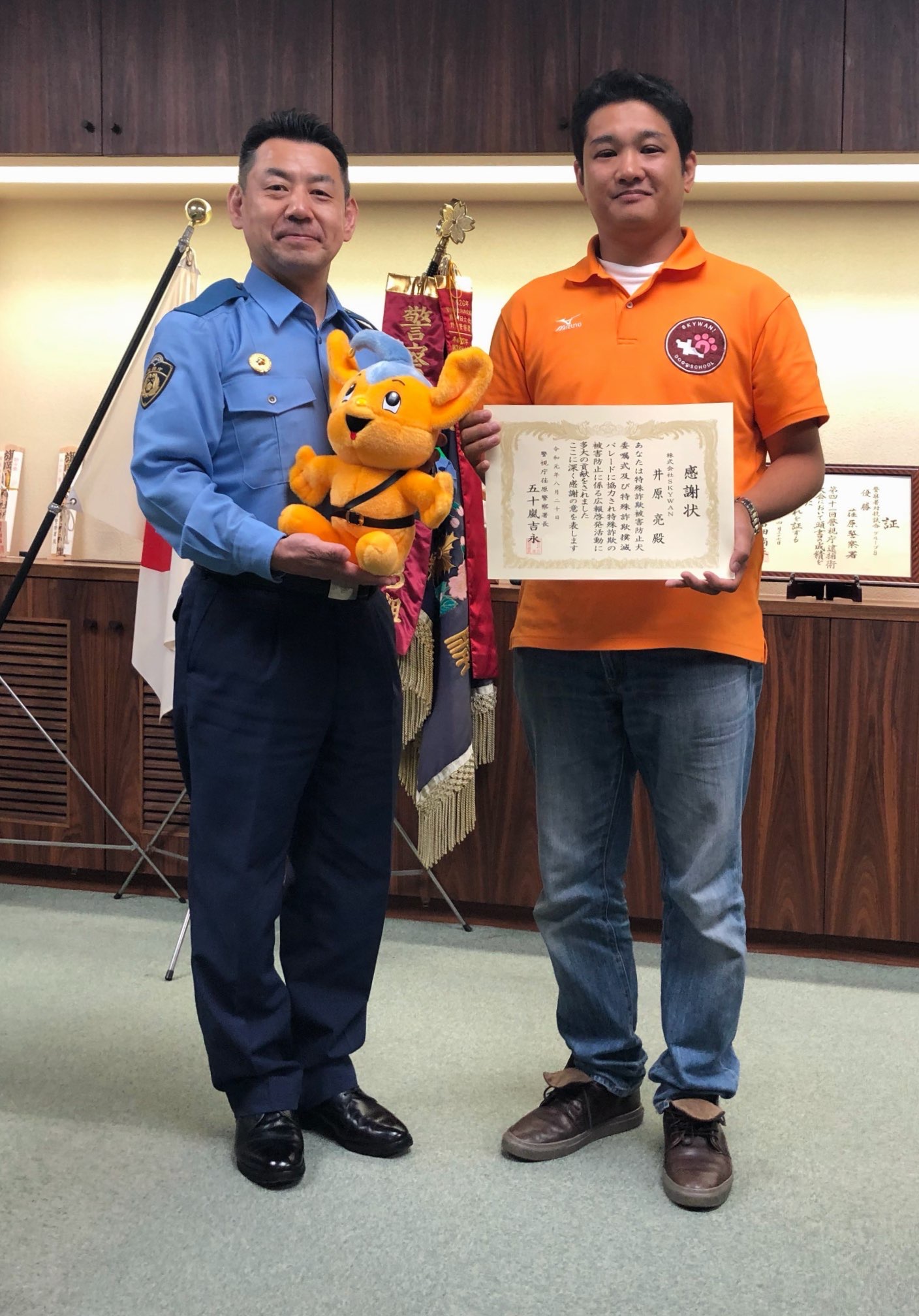 警察署長と井原亮さんが犬は電話に出ないワンの取り組みで撮影した写真
